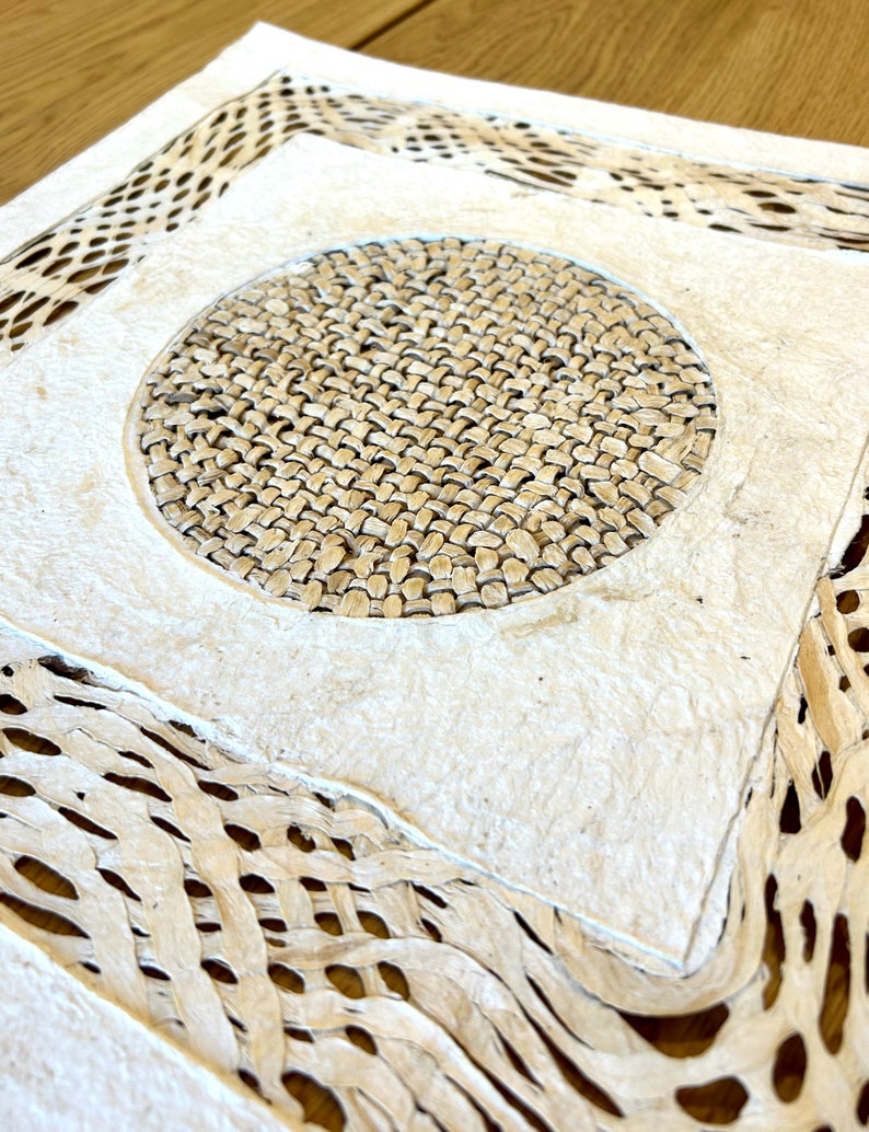 May include: A white paper with a woven design. The paper has a circular woven pattern in the center and a woven border around the edges.