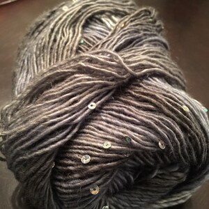 May include: A ball of grey yarn with subtle colour variations and embedded sequins. The yarn appears soft and textured, suitable for knitting or crochet projects. The sequins add a touch of sparkle to the yarn.