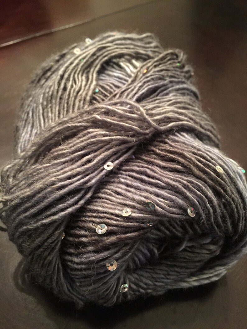 May include: A ball of grey yarn with subtle colour variations and embedded sequins. The yarn appears soft and textured, suitable for knitting or crochet projects. The sequins add a touch of sparkle to the yarn.