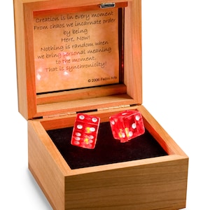 May include: A wooden box with a glass lid, containing two red dice with white dots. The box is open and the dice are illuminated from within. The lid has a quote about synchronicity and the year 2006.