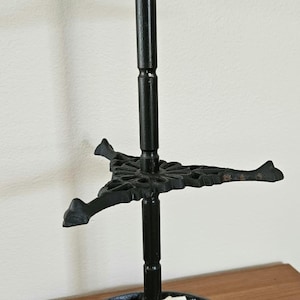 May include: A black cast iron tiered stand featuring a white and black cow figurine on the top tier. The base is a circular ring decorated with multiple white and black cow figures. The stand has a central vertical pole and two tiers.