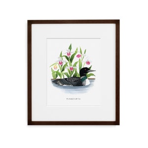 May include: A framed print of a watercolor painting depicting a loon swimming in a lake with pink and white lady slipper orchids. The text "Minnesota" is printed below the image.