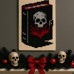 May include: A macrame wall hanging with a skull design, displayed above a mantel decorated with skulls, red ornaments, and a red bow. The skull design features a gray skull on a black background with red accents.