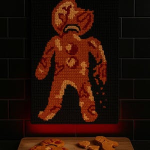 May include: A crochet wall hanging and gingerbread cookies on a wooden board. The wall hanging features a sad gingerbread man design in shades of orange and brown against a black background. The cookies are in the shape of gingerbread men, with some broken into pieces.
