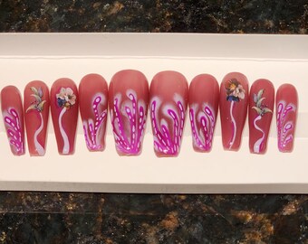 May include: Set of ten pink press-on nails with white and pink floral designs. The nails are long and have a coffin shape.