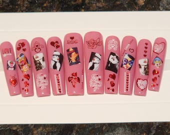 Puede incluir: Uñas postizas rosas y blancas con varios diseños que incluyen corazones, rosas y rostros de mujeres. Algunas uñas tienen el texto "Love You Forever" y "Love Love Love".