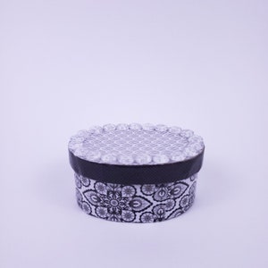 May include: A small round box with a black and white patterned design. The lid of the box is decorated with a row of white beads.