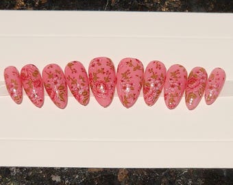 May include: A set of 10 pink almond-shaped press-on nails with a floral design.