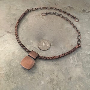 May include: A copper necklace with a twisted rope chain and a square pendant. The pendant is made of copper and has a hammered finish. The necklace is about 18 inches long and has a lobster clasp closure.