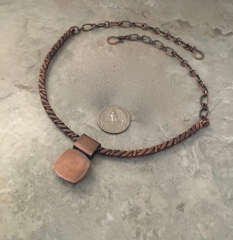 May include: A copper necklace with a twisted rope chain and a square pendant. The pendant is made of copper and has a hammered finish. The necklace is about 18 inches long and has a lobster clasp closure.