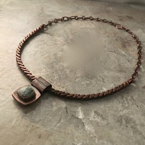 May include: A copper necklace with a twisted chain and a square pendant featuring a green stone.