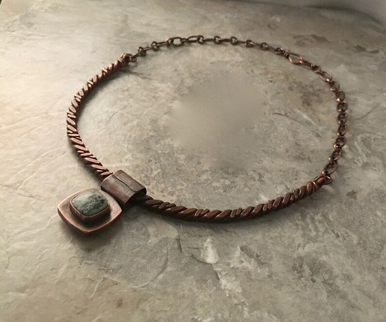 May include: A copper necklace with a twisted chain and a square pendant featuring a green stone.