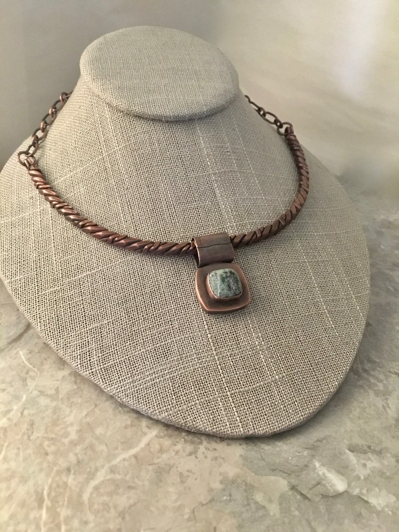 May include: A copper necklace with a twisted chain and a square pendant featuring a green stone.