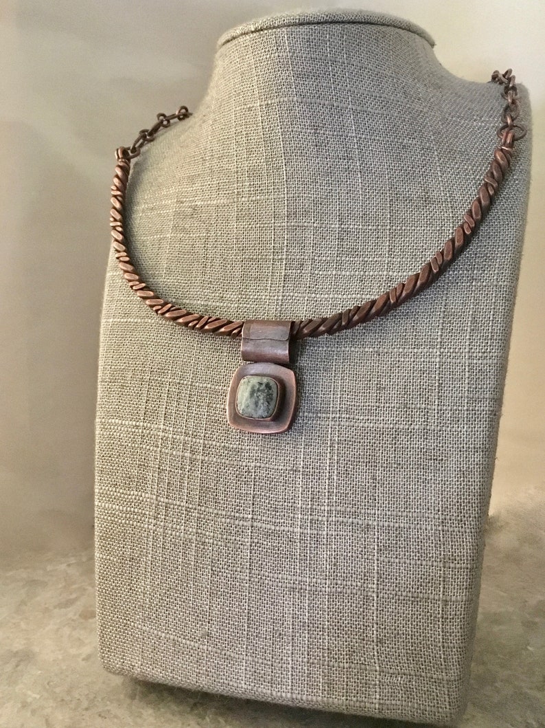 May include: A copper necklace with a twisted chain and a square pendant featuring a green and white stone.