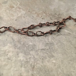 May include: A close-up of a copper chain necklace with a twisted copper pendant. The chain is made of oval links.