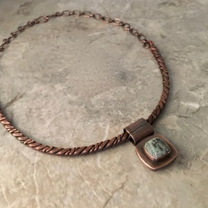 May include: A copper necklace with a twisted wire chain and a square pendant featuring a green stone.