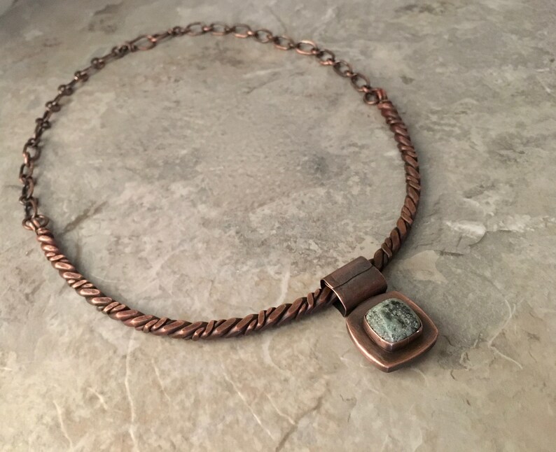 May include: A copper necklace with a twisted wire chain and a square pendant featuring a green stone.