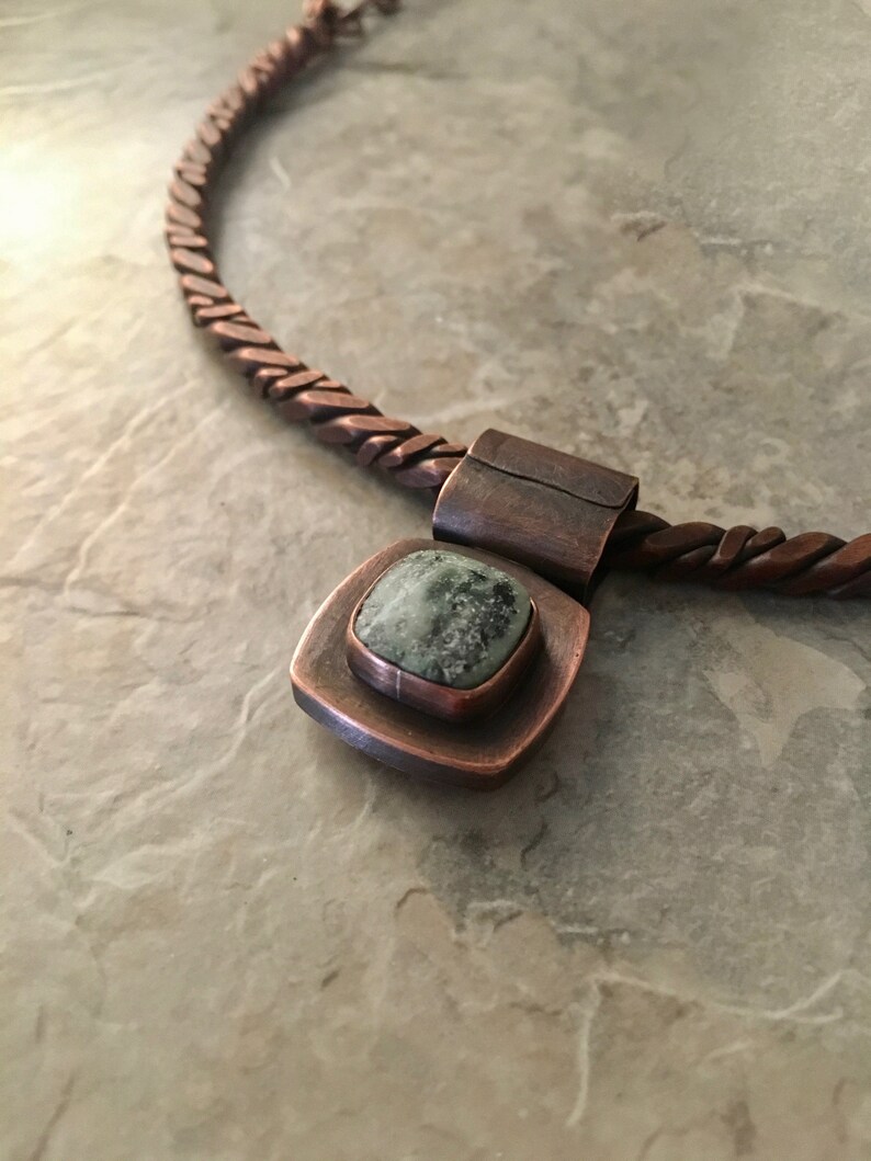 May include: A copper necklace with a braided chain and a square pendant featuring a green stone.