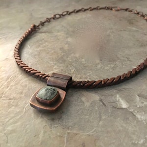 May include: A copper necklace with a braided chain and a square pendant featuring a green stone.