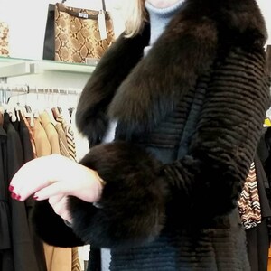 May include: A black fur coat with a large fur collar and cuffs. The coat has a ribbed texture and is belted at the waist.