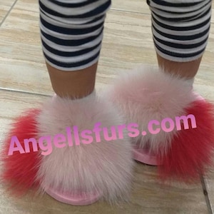 May include: Pink and red faux fur slippers with a fluffy pom-pom on each toe. The slippers are on a tiled floor. The text "Angelisfurs.com" is visible on the slippers.