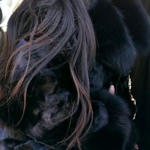 May include: A woman wearing a black fur coat with a large collar. She is wearing round sunglasses and has long black hair.