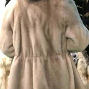 May include: A light brown fur coat with a large hood. The coat is made of soft, fluffy fur and has a simple, elegant design.