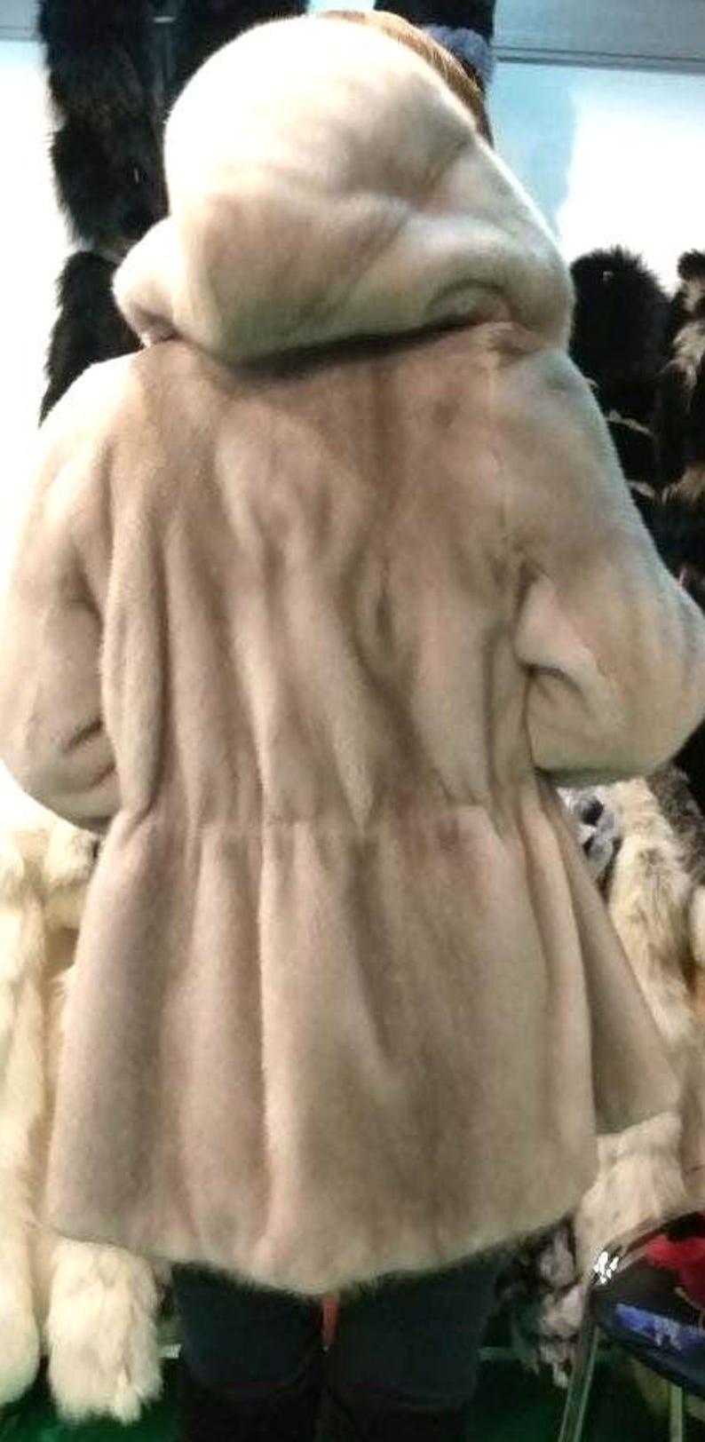 May include: A light brown fur coat with a large hood. The coat is made of soft, fluffy fur and has a simple, elegant design.