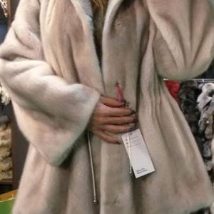 May include: A light beige fur coat with a zipper closure and a hood. The coat has a long, flowing style and is made of soft, luxurious fur.