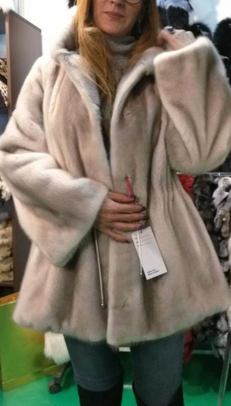 May include: A light beige fur coat with a zipper closure and a hood. The coat has a long, flowing style and is made of soft, luxurious fur.