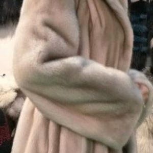 May include: A light beige fur coat with a large hood. The coat is made of soft, fluffy fur and has a long, flowing style.