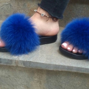 May include: A pair of blue faux fur slides with a black platform sole. The slides are made of soft, fluffy fur and have a comfortable fit.