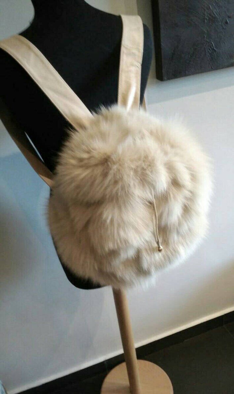 Puede incluir: Una mochila de piel sint&eacute;tica blanca con cierre de cord&oacute;n y correas de cuero.