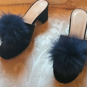 May include: Pair of black velvet heeled slippers with a fluffy blue pom-pom on the top of each slipper.