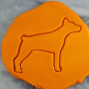 May include: A cookie cutter in the shape of a dog silhouette, pressed into orange fondant.
