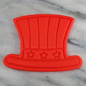 Könnte beinhalten: Roter Plastik-Ausstecher in Form eines traditionellen amerikanischen Zylinders mit drei Sternen auf der Banderole.