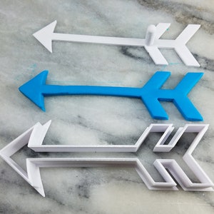 May include: Three arrow-shaped cookie cutters, one blue and two white. The white cutters are different sizes and have a more intricate design.