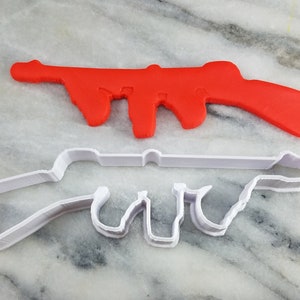 May include: Two cookie cutters shaped like guns. The top cutter is red plastic and the bottom cutter is white plastic.