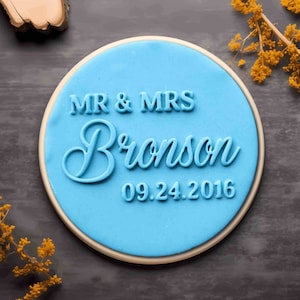May include: A light blue round cookie with white icing and the text "MR & MRS Bronson 09.24.2016" in blue icing.