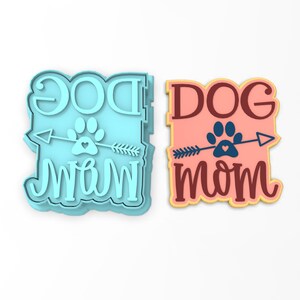 May include: Two cookie cutters, one blue and one pink, with the text "DOG MOM" and a paw print with an arrow.