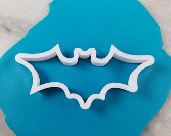 Könnte beinhalten: Weißer, plastikförmiger Ausstecher in Form einer Fledermaus auf blauem Fondant-Hintergrund.