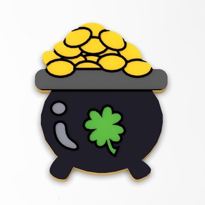 May include: A black pot with a gold coin design on top and a green shamrock on the front. The pot has a gold rim and three legs.