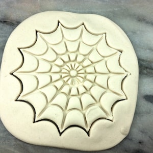 May include: A white clay mold with a spiderweb design. The mold is used to create cookies or other baked goods.