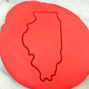 May include: A red cookie dough sheet with a cookie cutter in the shape of the state of Illinois.