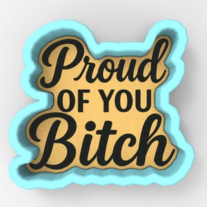 May include: A light blue cookie cutter with the words "Proud of You Bitch" in black script. The interior is a light tan color. The cookie cutter has a unique shape.