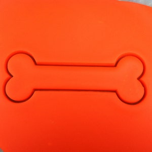 Op de afbeelding: Een feloranje siliconen koekjesvormpje in de vorm van een hondenbot.