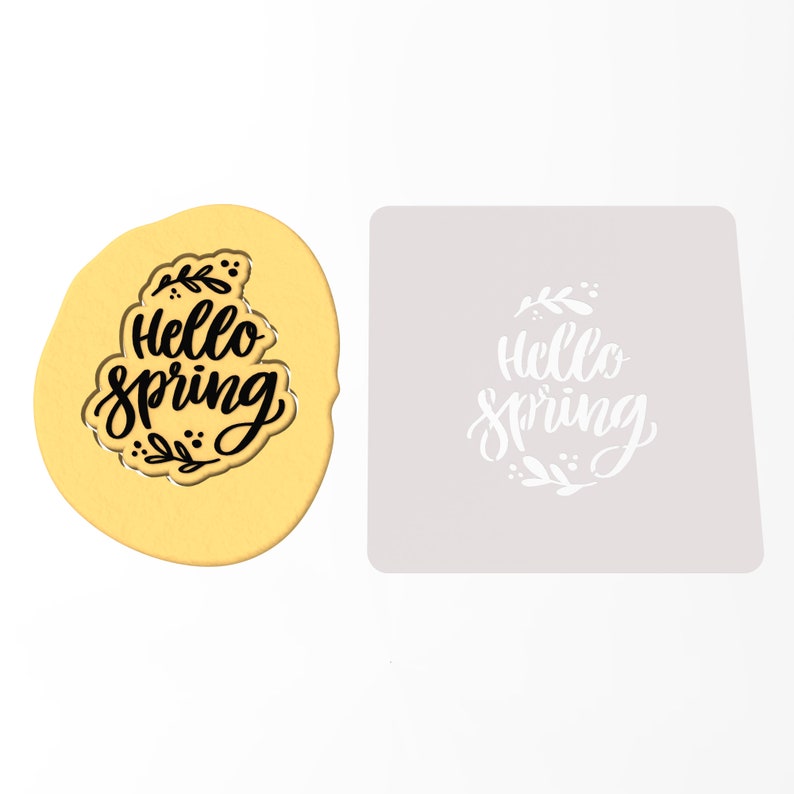 Op de afbeelding: Een gouden koekjesvormpje met de woorden "Hello Spring" in zwarte schrijfletters en een bloemmotief. Naast het koekjesvormpje is een witte sjabloon met hetzelfde ontwerp te zien.