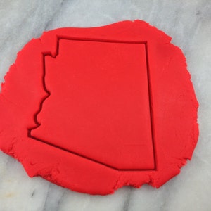 May include: Red cookie dough with a cookie cutter shaped like the state of Arizona.