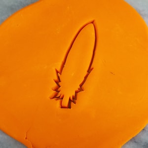 以下が含まれることがあります： オレンジ色のフォンダンに、羽根の形をしたクッキーカッターの跡があります。羽根は、より濃いオレンジ色で縁取られています。