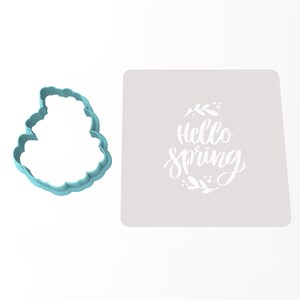 Op de afbeelding: Een lichtblauwe koekjesvormer in de vorm van een wolk met de woorden "Hello Spring" in een witte sjabloon op een grijze achtergrond.